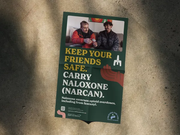 Image of a poster with two males sitting on a couch and one handing the other Naloxone